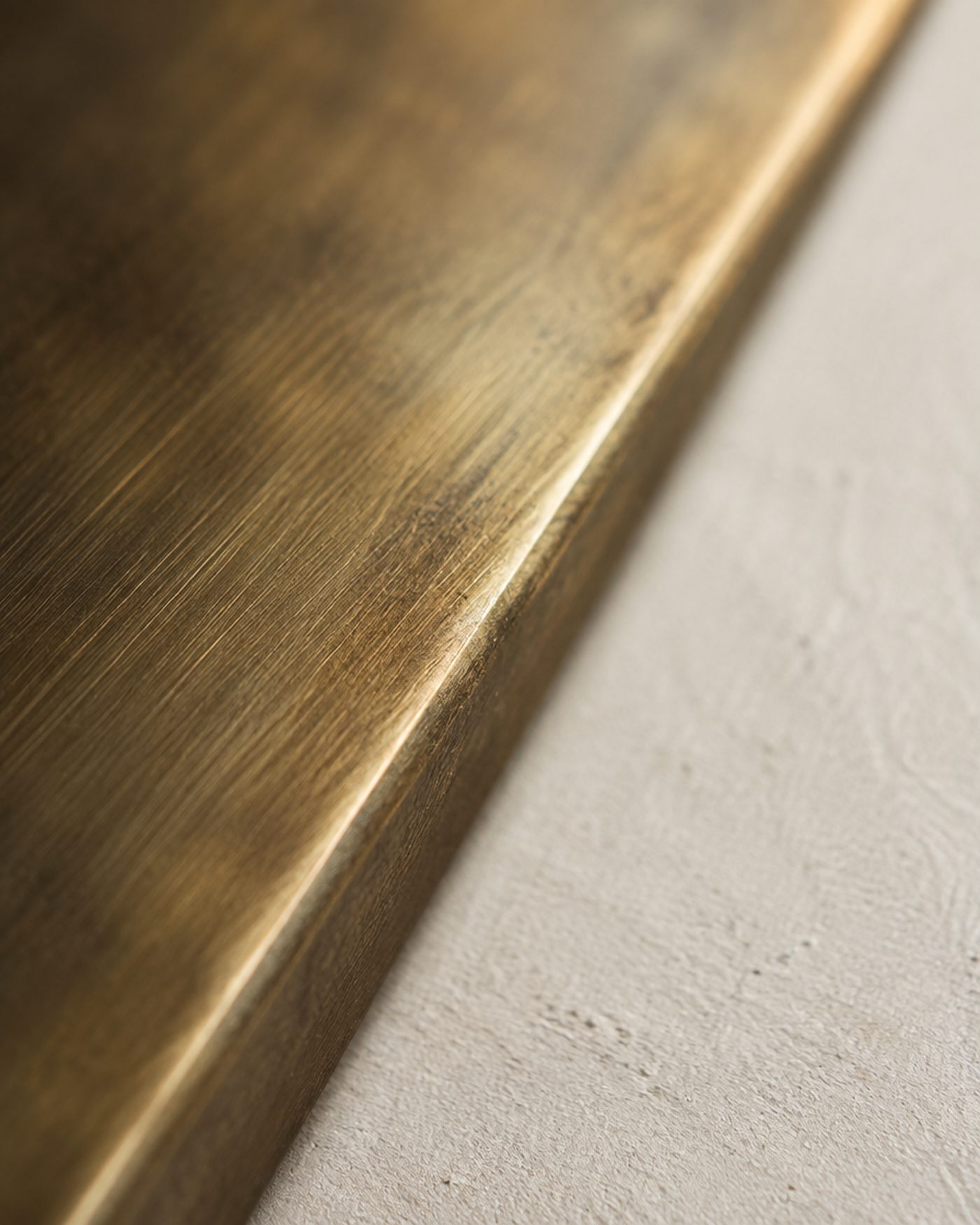Macro detail of an unlacquered brushed brass edge meeting matte plaster.